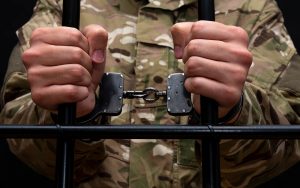 A handcuffed soldier behind the bars against a black background.